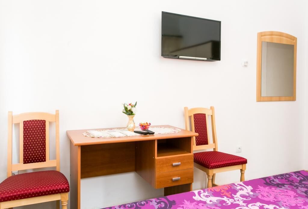 Une pièce avec un bureau en bois, deux chaises, une télévision et un miroir.