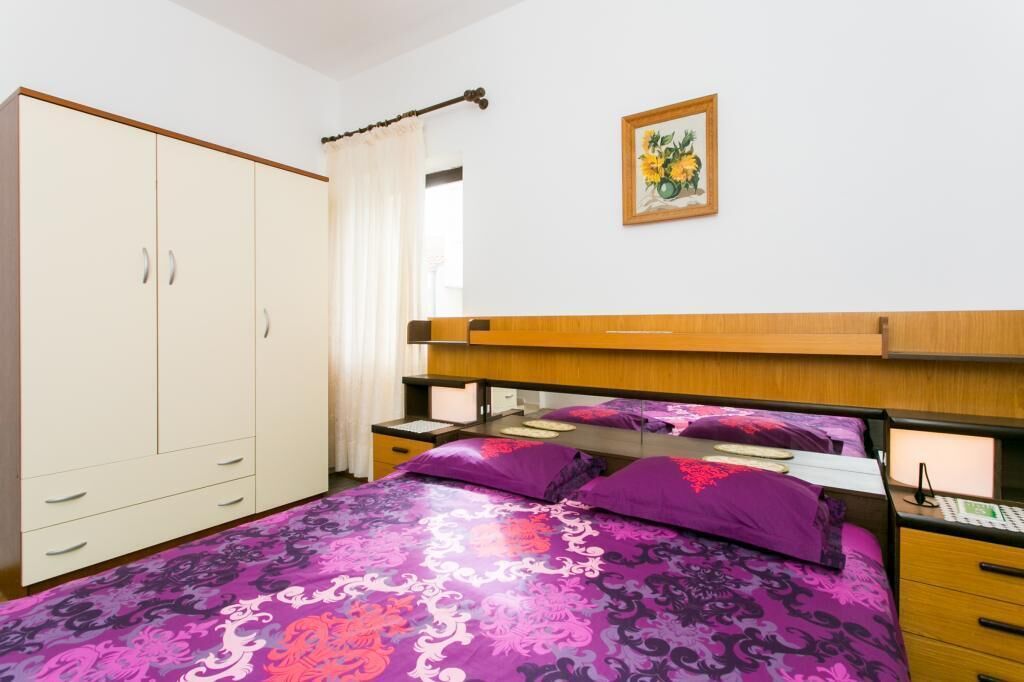 Een slaapkamer met een bed, een kledingkast, een nachtkastje en een schilderij aan de muur.