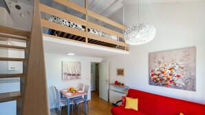 A modern apartment with a dining area, a red sofa, and a loft bedroom with a wooden staircase.