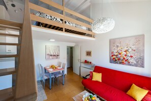 A modern apartment with a dining area, a red sofa, and a loft bedroom with a wooden staircase.