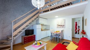 A modern apartment with a staircase, a kitchen, a dining area, and a living room with a red sofa.