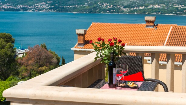 A balcony with a table set for two, overlooking a lake with mountains in the background.