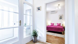Ein Flur, der in ein Schlafzimmer mit Bett, Zimmerpflanze und einer Glastür mit Verglasung führt.