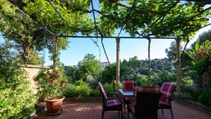 Eine überdachte Terrasse mit Ziegelboden, Körbchenmöbeln aus rot und schwarz sowie einem Tisch.