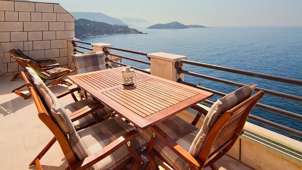 A wooden table and chairs on a balcony with a view of the sea and distant mountains. - Big Blue Apartments - One-Bedroom Apartment with Balcony and Sea View (Big Blue 2) (Dubrovnik)