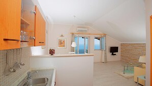 A modern kitchen with a built-in sink, wooden cabinets, and a view of the sea through an open door. - Big Blue Apartments - One-Bedroom Apartment with Balcony and Sea View (Big Blue 2) (Dubrovnik)