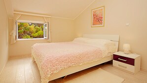 A bedroom with a bed, a nightstand, a lamp, a window with curtains, and a painting on the wall. - Big Blue Apartments - One-Bedroom Apartment with Balcony and Sea View (Big Blue 2) (Dubrovnik)