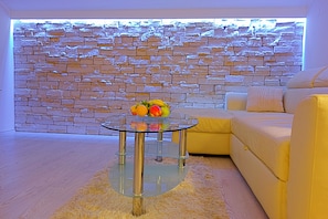 A modern living room with a glass coffee table, a stone wall, and a yellow sofa.