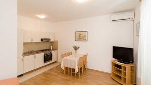 A compact kitchen with a dining table and chairs, a flat-screen TV, and an air conditioning unit.