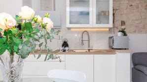 Une cuisine moderne avec des armoires blanches, un mur d’accent en pierre, un four à micro-ondes encastré et un vase rempli de fleurs posé sur le comptoir.