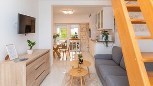 Un salon moderne avec un canapé, un téléviseur fixé au mur, un bureau en bois et un escalier.