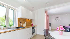 A modern kitchen with white cabinets, a wooden countertop, and a built-in oven. There is a dining area with a glass table and chairs, and a pink vase with flowers. - Apartments Sunny Days - Comfort Two Bedroom Apartment with Terrace and Sea View (A1) (ST) (Milna)