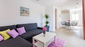 A modern living room with a grey sofa, a white coffee table, and a pink rug. There is a dining area with a table and chairs in the background. - Apartments Sunny Days - Comfort Two Bedroom Apartment with Terrace and Sea View (A1) (ST) (Milna)