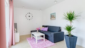 A modern living room with a grey sofa, a white coffee table, a large potted plant, and a wall clock. - Apartments Sunny Days - Comfort Two Bedroom Apartment with Terrace and Sea View (A1) (ST) (Milna)