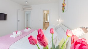 A hotel room with a bed, a bedside table, a TV mounted on the wall, and a door leading to a bathroom. - Apartments Sunny Days - Comfort Two Bedroom Apartment with Terrace and Sea View (A1) (ST) (Milna)