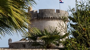 Ein historischer Steinturm mit einer Flagge, umgeben von viel Grün.