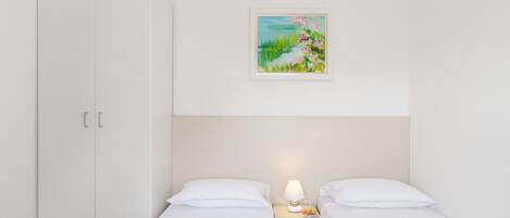 Una habitación de hotel con dos camas individuales, un armario, una mesita de noche con lámpara y un cuadro en la pared.