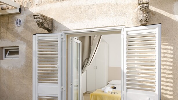 Ein Zimmer mit einem Bett, einem Fenster mit Jalousien und einer Tür zu einem anderen Raum.
