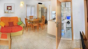 Ett kompakt bostadsutrymme med en matplats, en soffa, ett litet bord och ett litet kök.