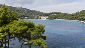 Vista costera con aguas azules cristalinas, una playa arenosa y colinas verdes al fondo.