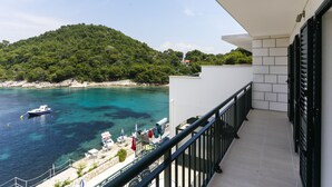 Un balcón con vista a una zona costera, incluyendo un barco en el agua y una colina con árboles.