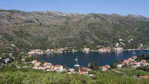 Un pueblo costero con casas a lo largo de la orilla, un lago azul cristalino y colinas al fondo.