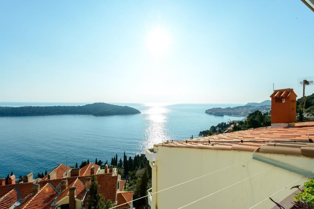 A coastal view with terracotta-roofed buildings overlooking a calm sea.