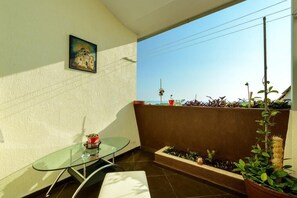 Een balkon met een glazen tafel en stoelen, een bloempot en uitzicht op een toren.