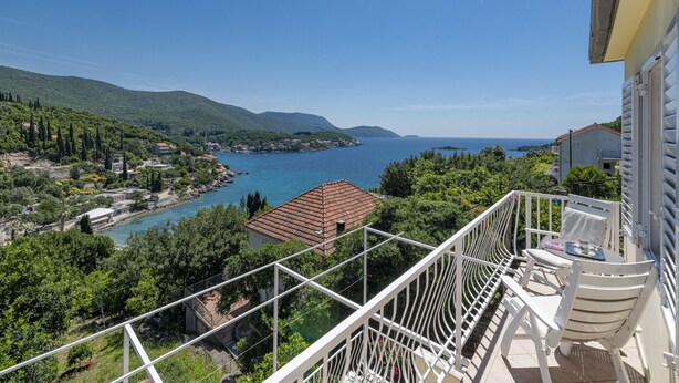 Ein Balkon mit weißen Geländern, der auf eine Küstenlandschaft mit freiem Blick auf das Meer und umliegendes Grün blickt.