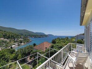 A balcony with white railings overlooking a coastal area with a clear view of the sea and surrounding greenery.