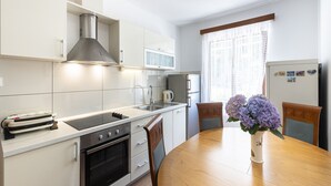 A modern kitchen with white cabinets, a stainless steel range hood, a microwave, and a refrigerator. There is a dining table with chairs and a vase of flowers. - Guest House Rooms Rose - Romantic Double Room with Balcony and Sea View (No.2) (Molunat)