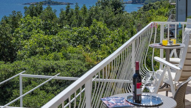A balcony with a table set for two, overlooking a coastal landscape with trees and the sea. - Guest House Rooms Rose - Romantic Double Room with Balcony and Sea View (No.2) (Molunat)