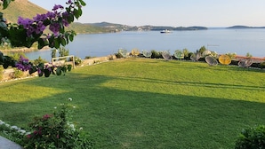 Eine grüne Rasenfläche mit Blick auf ruhiges Wasser und ferne Hügel.