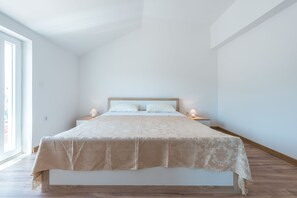 A minimalist bedroom with a large bed, two bedside tables, and a large window providing natural light.