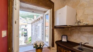Una cocina con pared de piedra, encimera de madera, refrigerador blanco y vistas a edificios desde una puerta abierta.