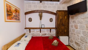 Un dormitorio con pared de piedra, cabecera de madera, televisor montado en la pared y cama con manta y toallas rojas.