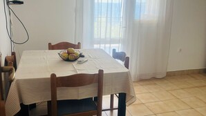 Uma sala de jantar com uma mesa, cadeiras, uma fruteira e uma televisão na parede.