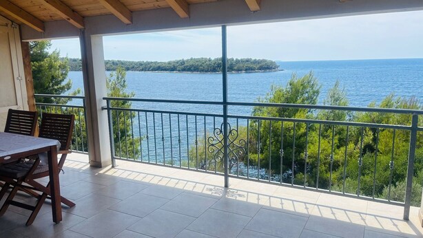 Uma varanda com vista para o mar, uma mesa com cadeiras e um corrimão.