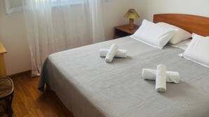 Cama bem arrumada com roupa de cama e toalhas brancas, abajur e janela com cortinas finas.
