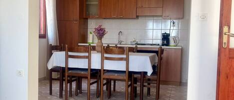 Een eethoek met een tafel en stoelen, een keuken met houten kasten, en een betegelde vloer.