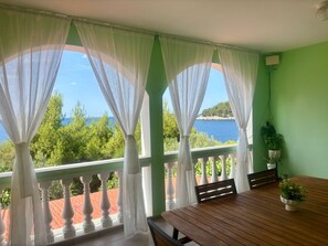 A balcony with white curtains, a wooden table, and a potted plant.