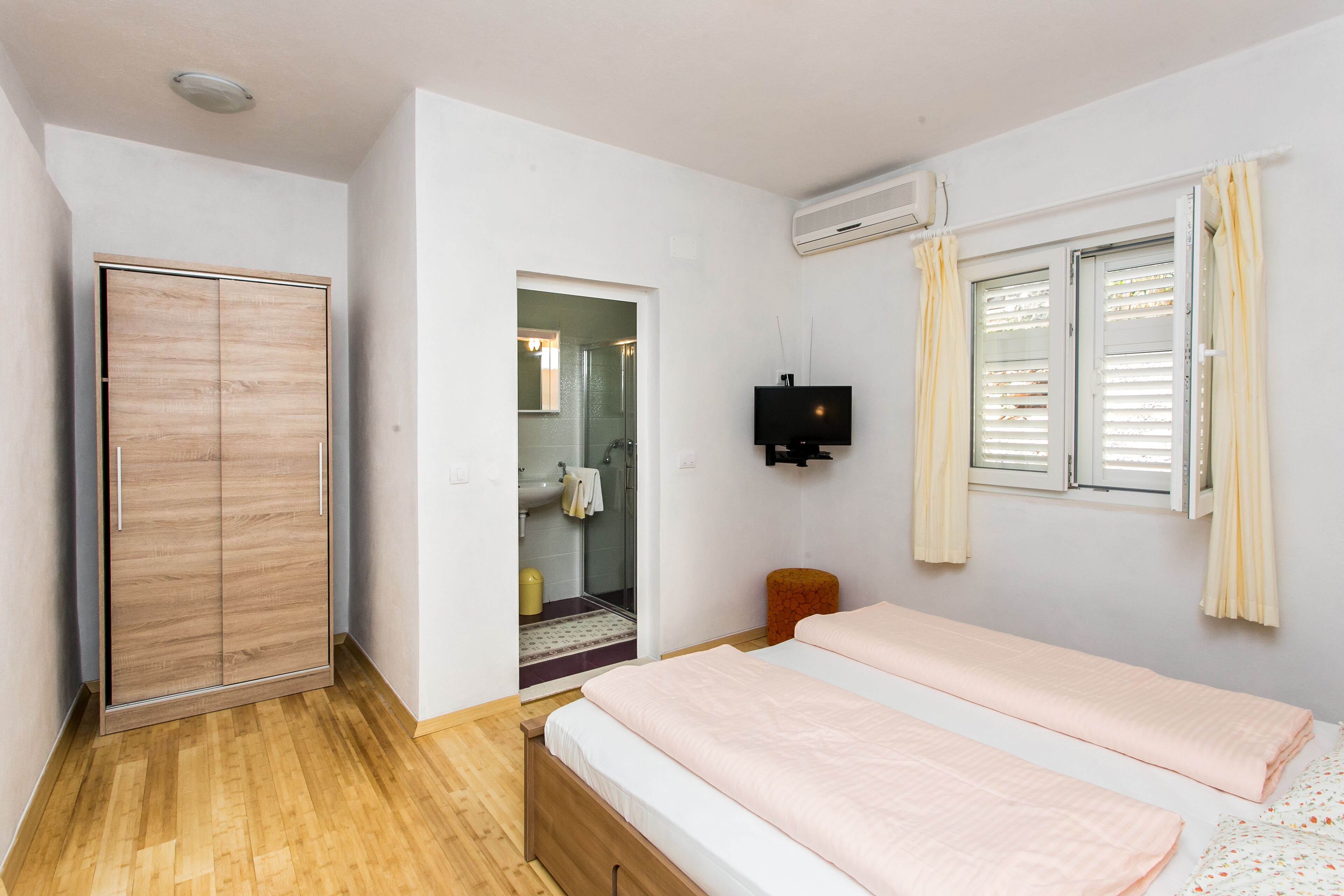 A bedroom with two beds, a wardrobe, a television, and a window with curtains.