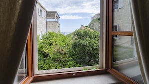 A room with a view of a stone building and greenery through a window.