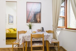 Un coin repas avec une table dressée pour deux personnes, une plante en pot et un tableau encadré au mur.