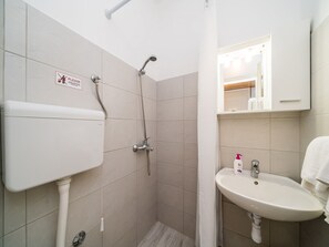 Een badkamer met douche, toilet, wastafel en spiegel.