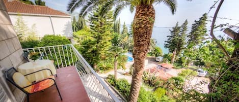 A balcony with a table and chairs, overlooking a pool and lush greenery.