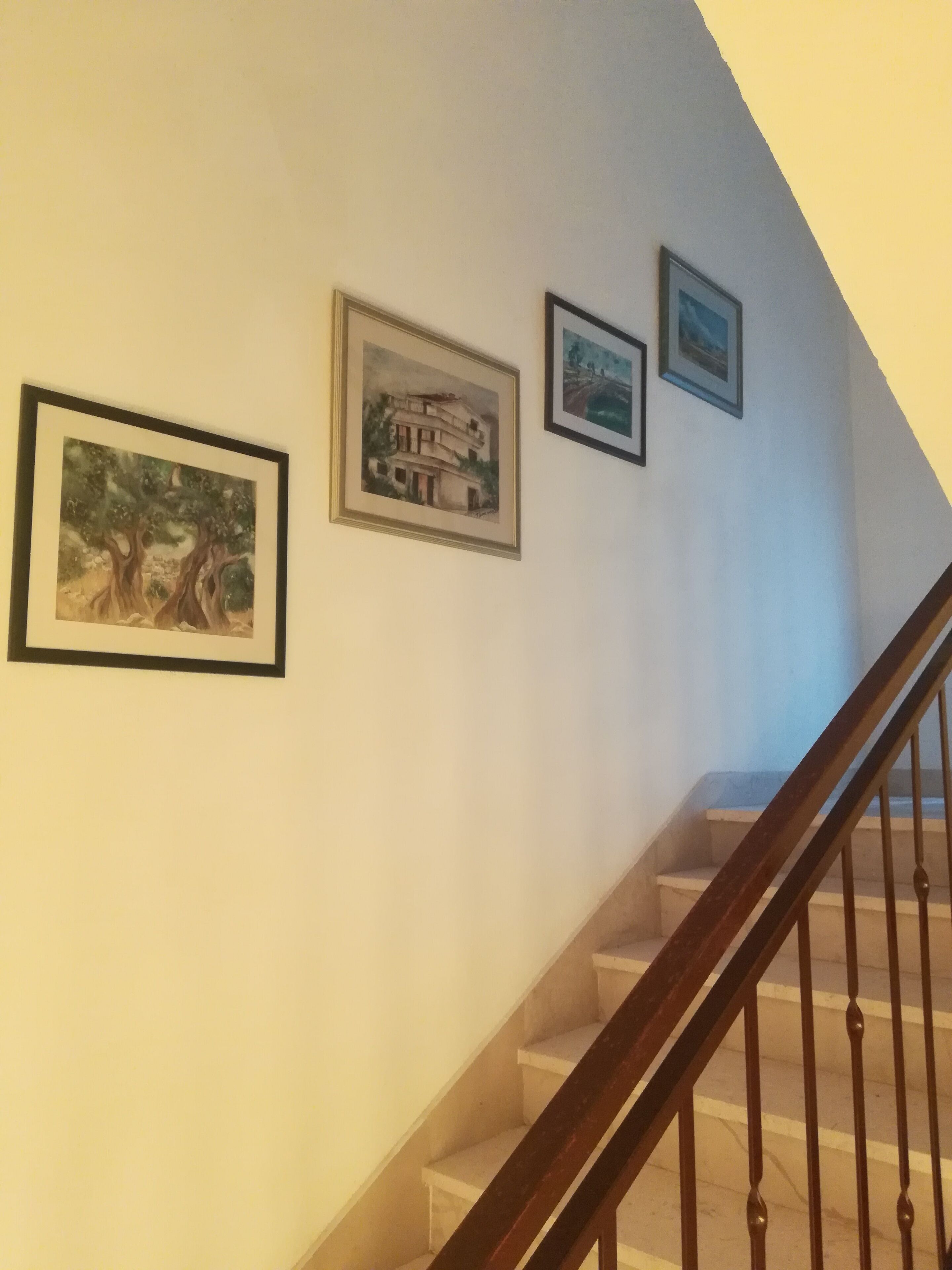 A staircase with a wooden handrail and a white wall with three framed pictures.