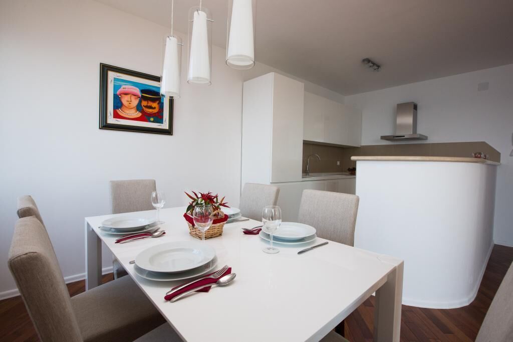 A dining area with a white table set for four, including plates, cutlery, and glasses. There is a small plant on the table, and a framed picture hangs on the wall.