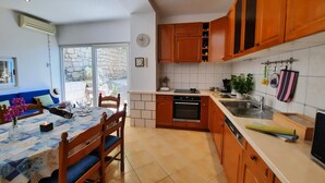 Una cocina con armarios de madera, una mesa de comedor con sillas, un horno empotrado y una ventana con vista a un muro de piedra.