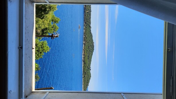 Vista desde una ventana sobre un cuerpo de agua con una isla distante y una orilla bordeada de árboles.